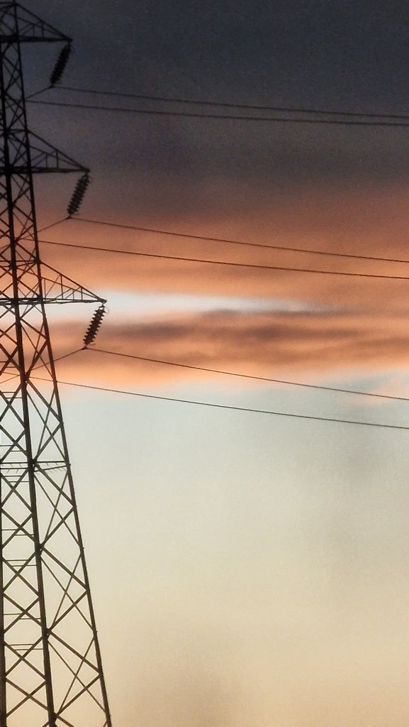 A stunning sunset casts orange hues over a silhouette of a transmission tower and power lines.