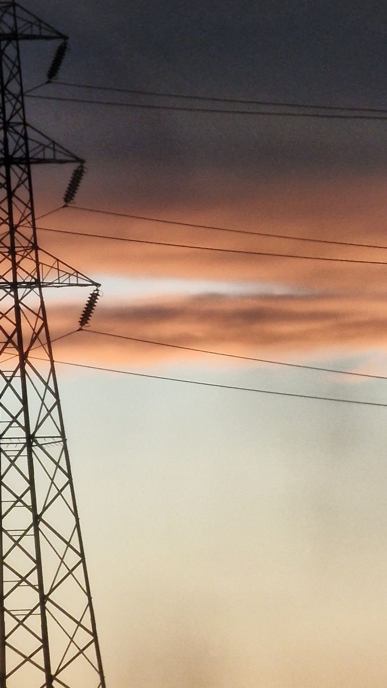 A stunning sunset casts orange hues over a silhouette of a transmission tower and power lines.