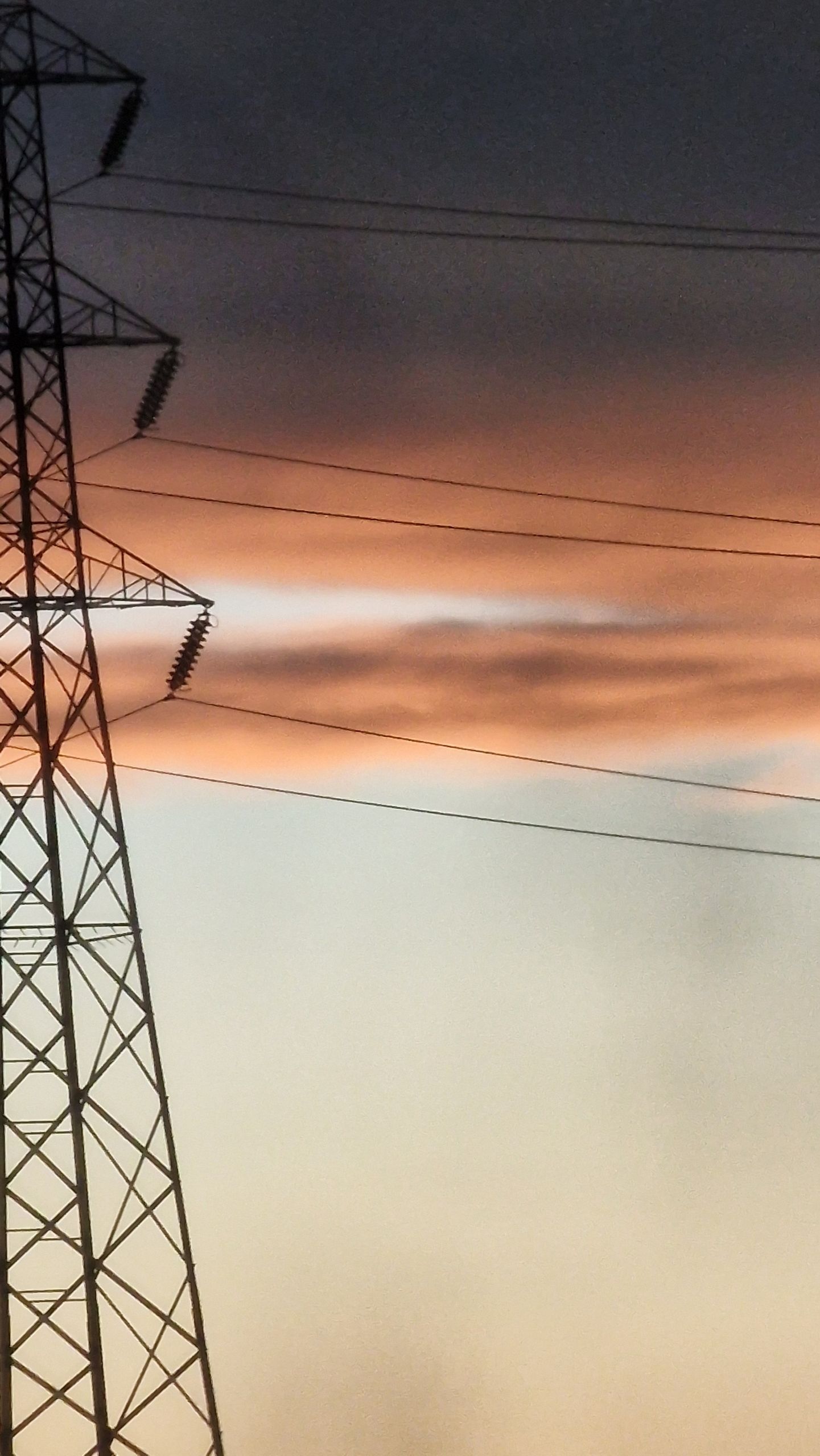 A stunning sunset casts orange hues over a silhouette of a transmission tower and power lines.