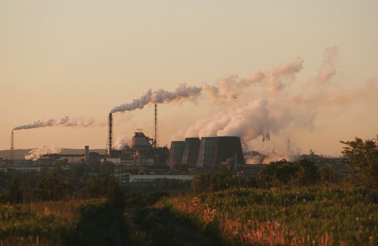 Factory chimneys releasing smoke into the sky at sunset, highlighting industrial pollution.