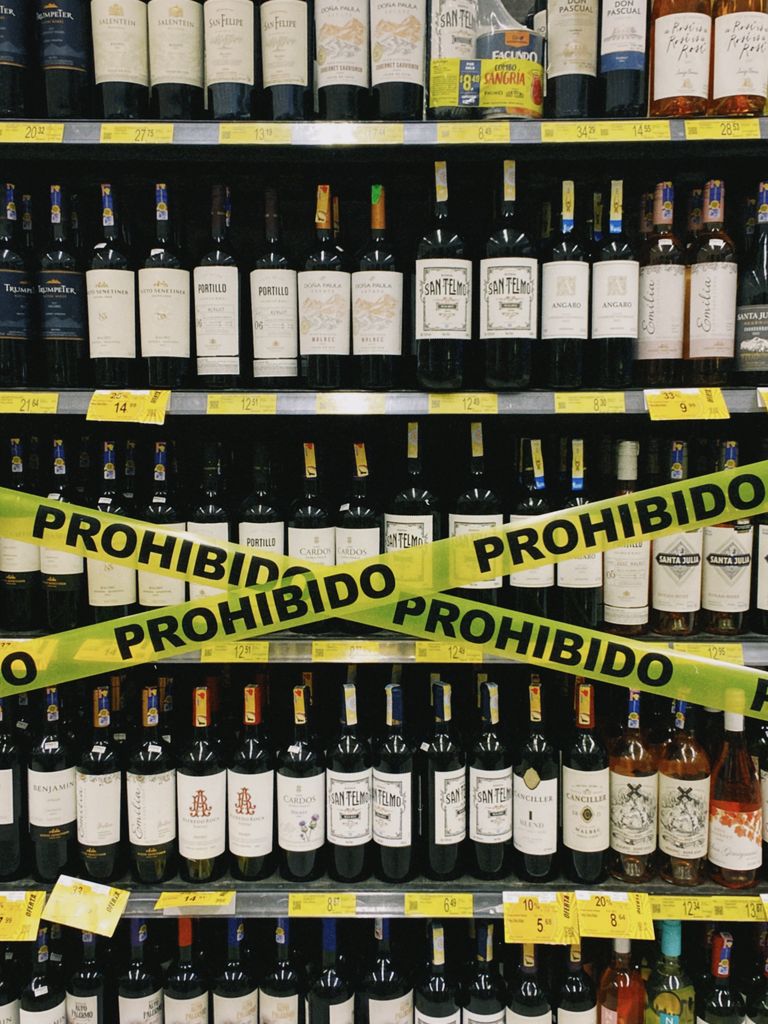 Wine bottles on shelves with prohibition tape in a store setting.